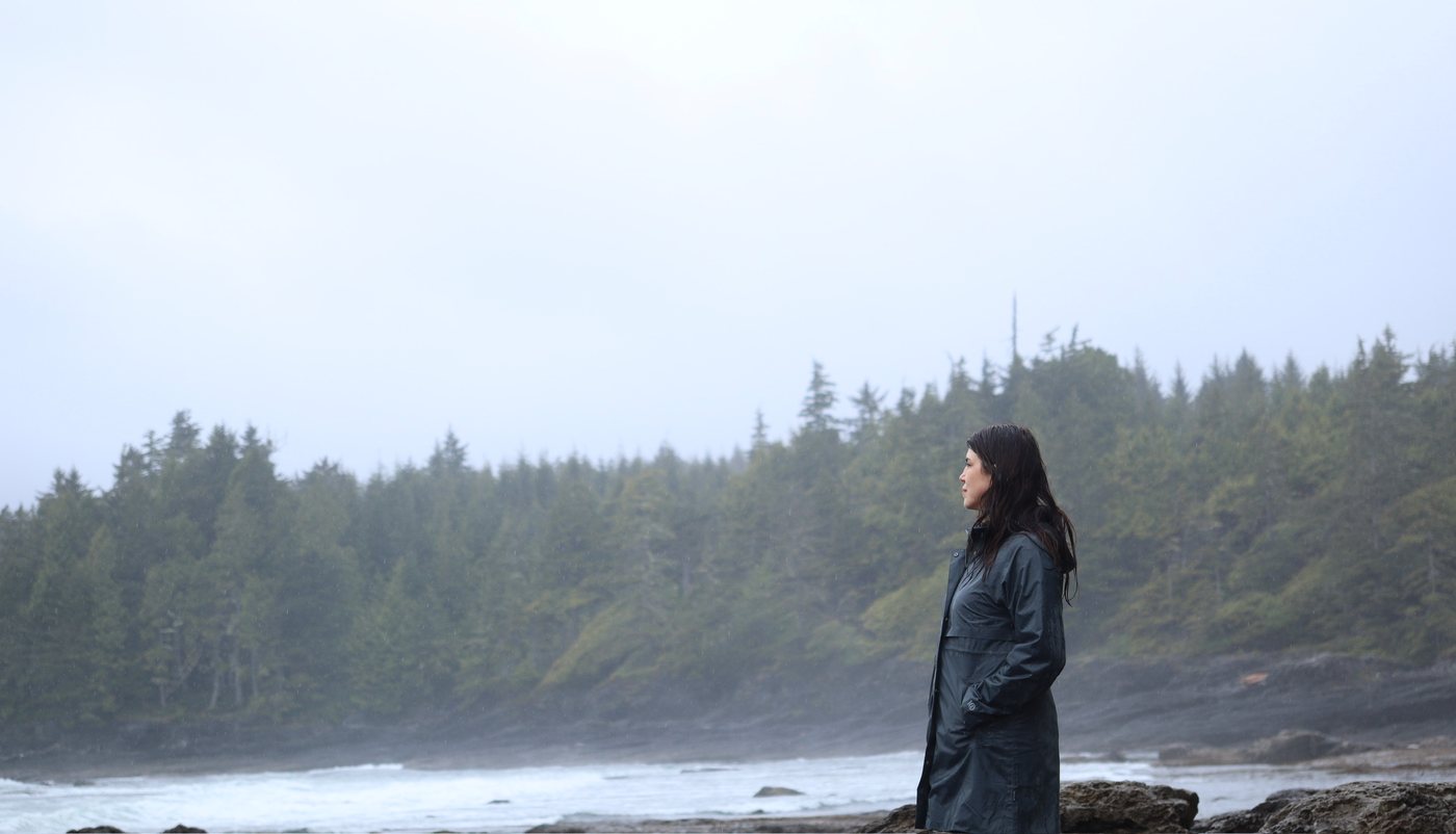 Brandy Nielson standing on a misty Vancouver Island shoreline, looking out toward the forest