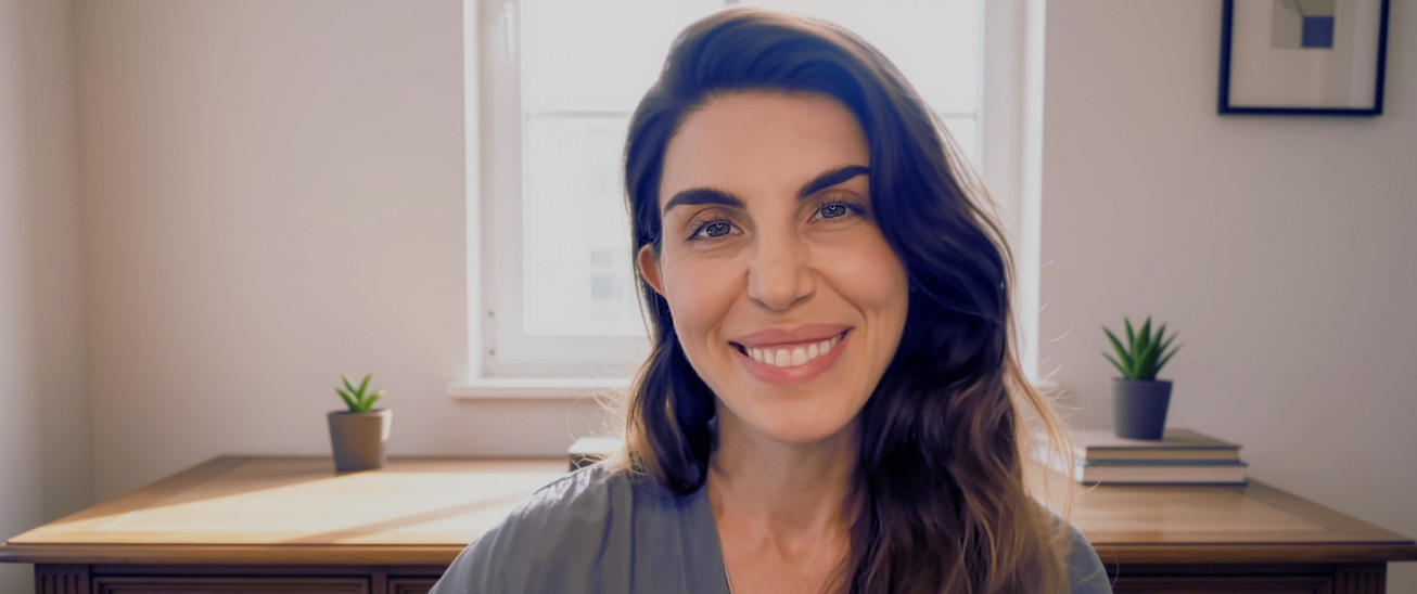 Brandy Nielson smiling warmly, seated at a wooden desk in a bright room