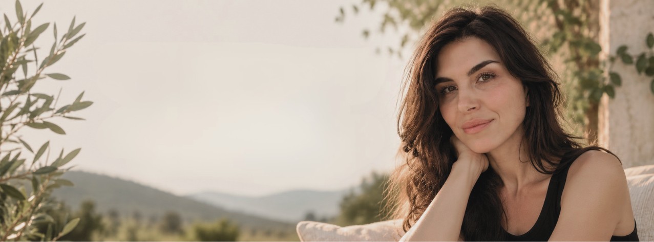 Brandy Nielson resting her chin on her hand in warm evening light, hills and olive branches behind her