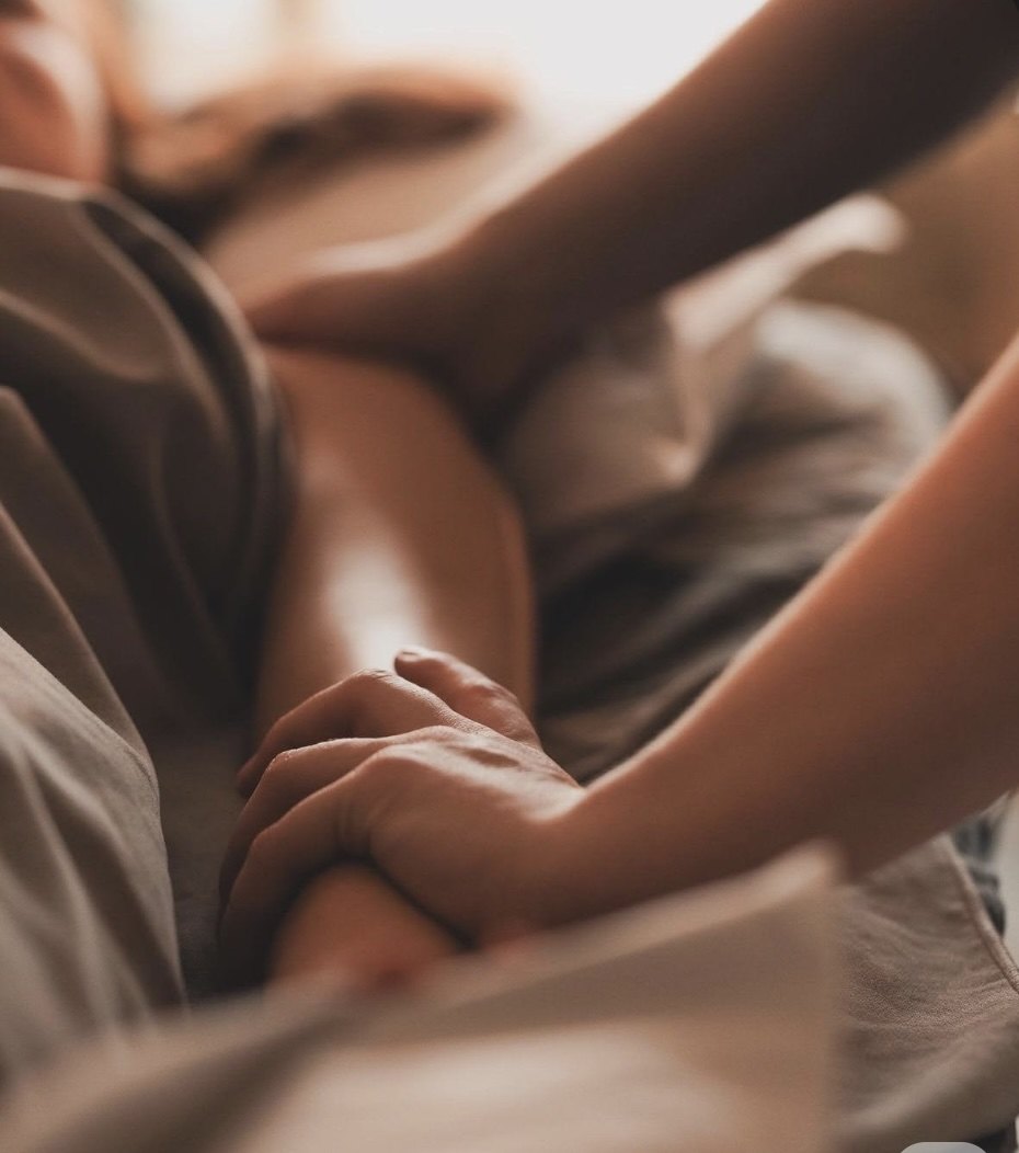 A practitioner's hands resting gently on a person lying under soft linen during a Reiki session