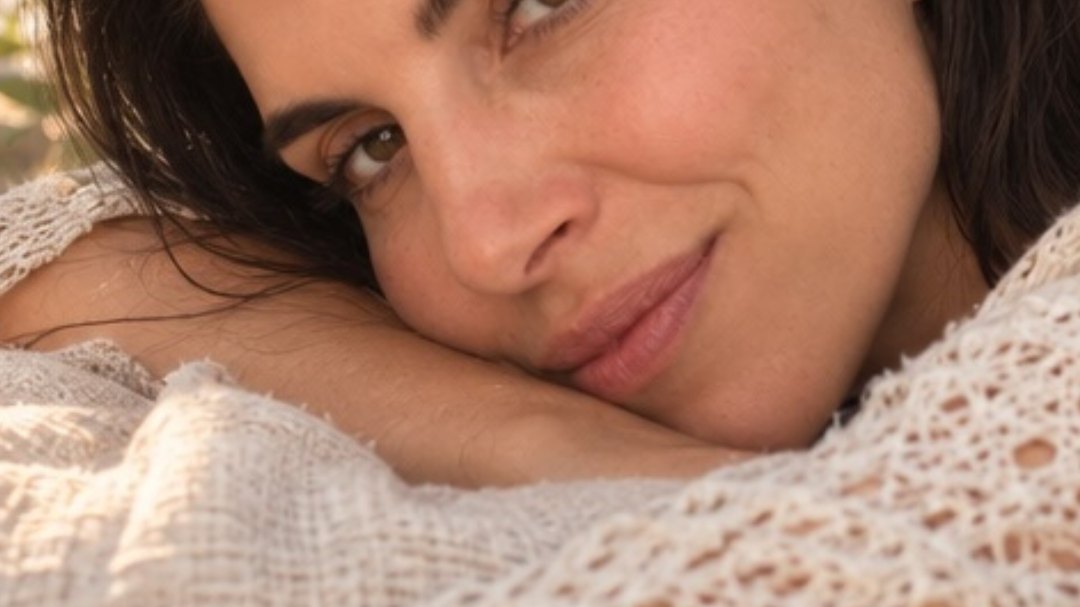 Brandy resting her head on her arm, wrapped in a soft cream crochet knit, warm light across her face